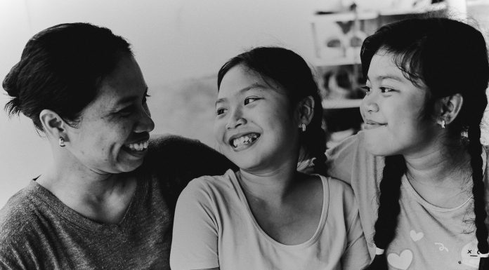 Back-to-School Health: Everyday Habits to Keep Mom Energized and Injury-Free Black and white image of a smiling mom sitting on the floor with her children in a cozy living room, showing a moment of connection and balance, reflecting Mom Back to School health.